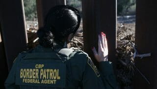 U.S. Border Patrol women looking through a fence