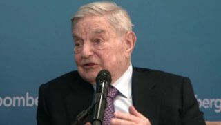 A seated Soros speaks into a microphone