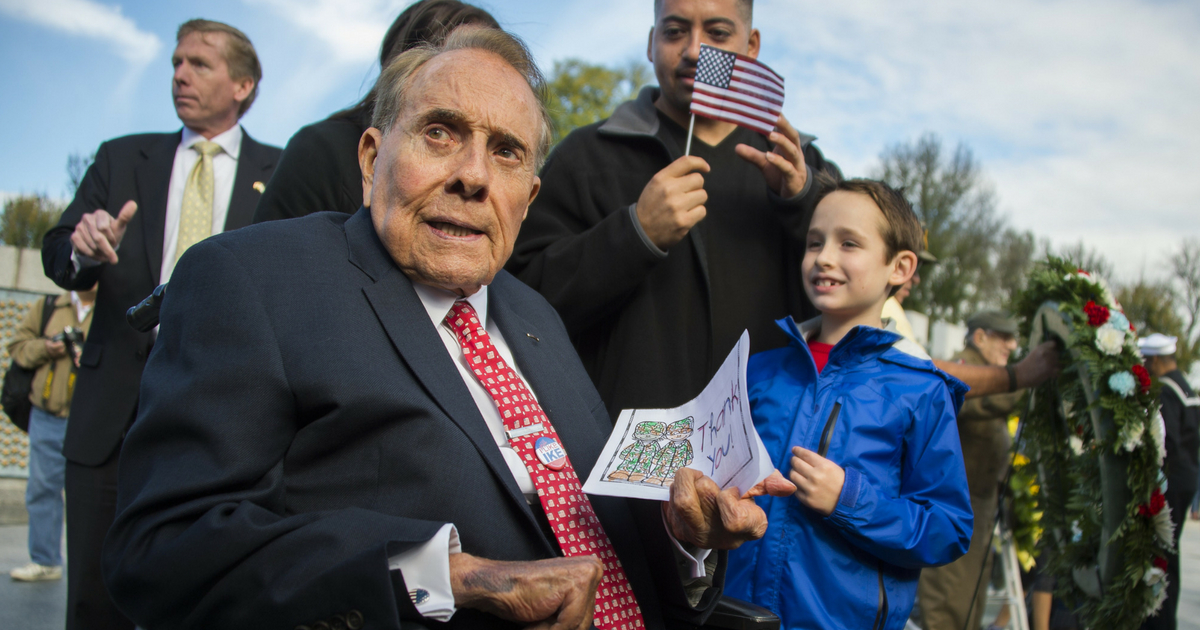 Former US Senator and World War II veteran Bob Dole (C) holds a card given to him by a young boy (R) after laying a wreath at the World War II Memorial on Veteran's Day in Washington, DC, November 11, 2015.