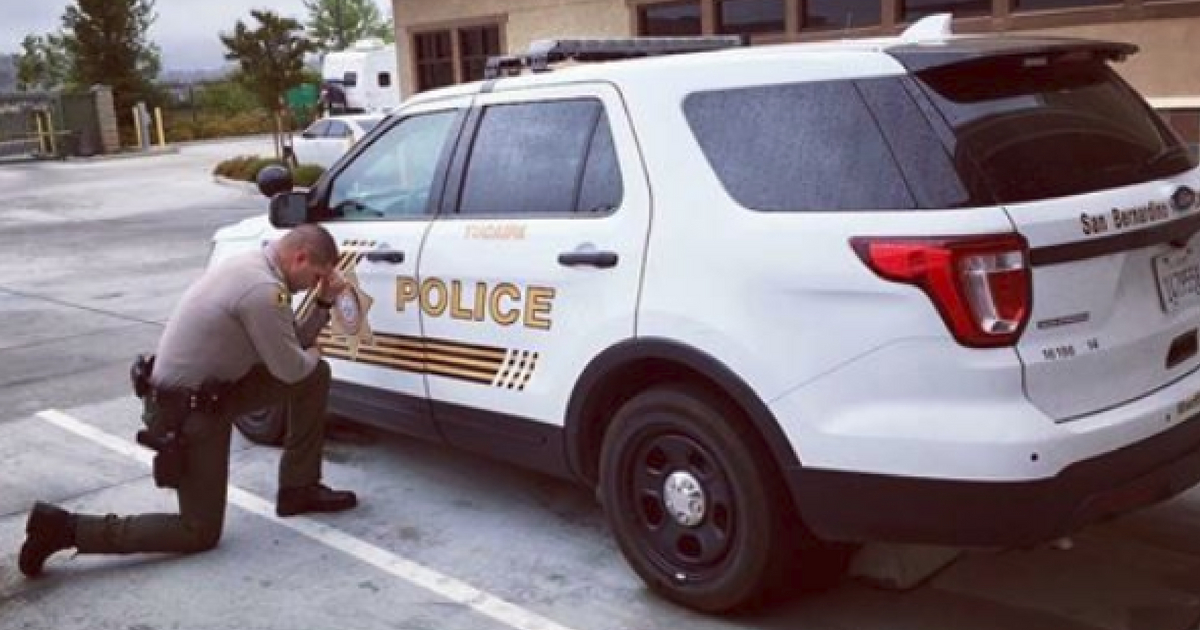 Officer kneels in prayer in front of cruiser