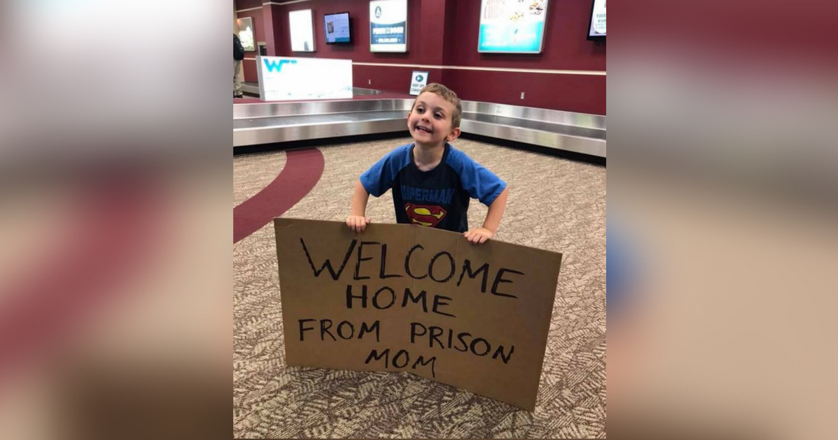 Young boy welcomes mom home from business trip with a sign that reads 'welcome home from prison mom.'
