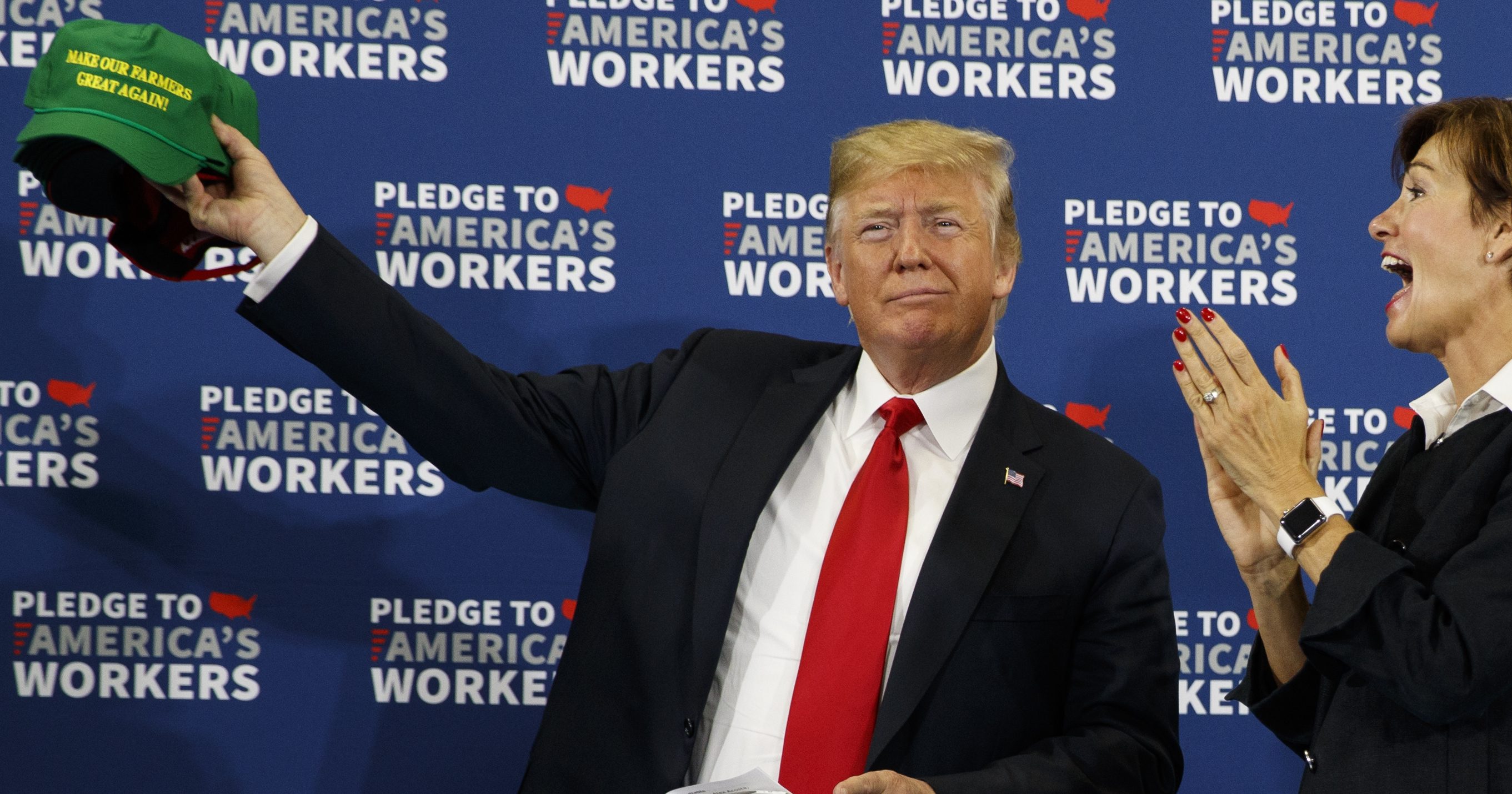 Gov. Kim Reynolds, R-Iowa, center, look on as President Donald Trump holds up a "Make Our Farmers Great Again" hat during a roundtable discussion on workforce development at Northeast Iowa Community College, Thursday, July 26, 2018, in Peosta, Iowa.