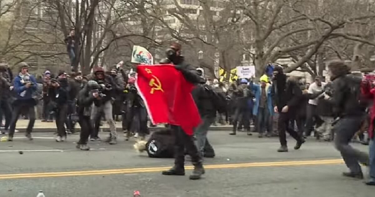 Mob led by man carrying hammer & sickle banner