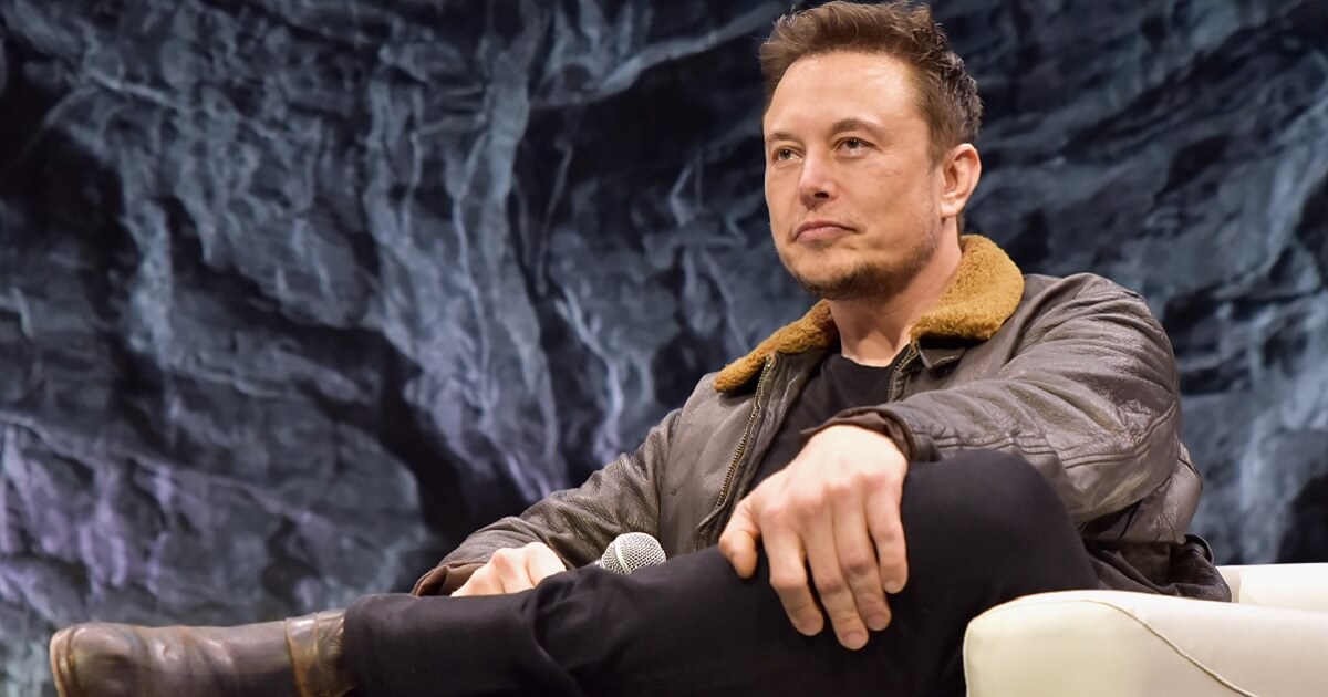 Standalone photo of Tesla co-founder Elon Musk seated on a couch onstage.