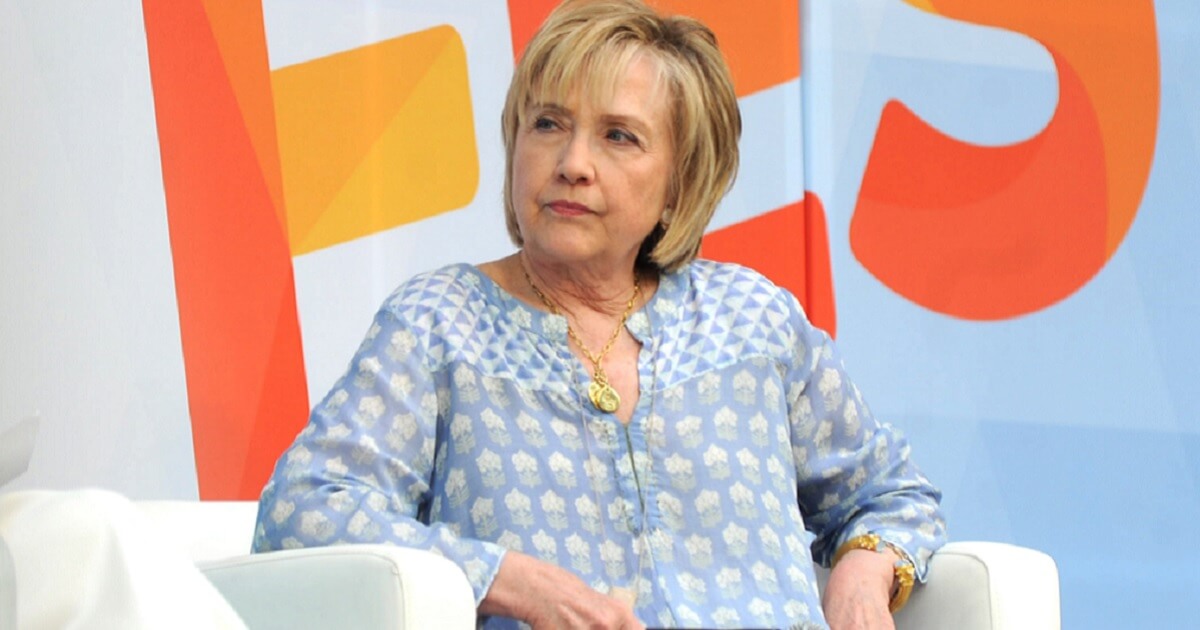 Hillary Clinton scowling to her left wearing what looks like a flowered hospital gown.