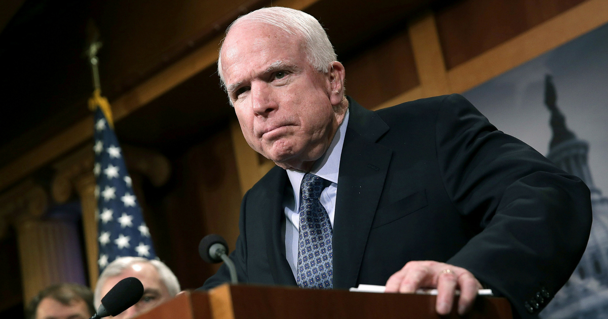 Sen. John McCain leans over a podium during a press conference.
