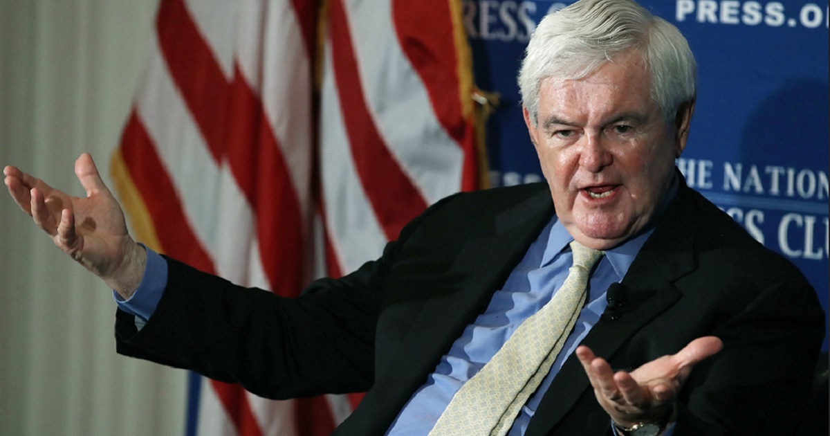 Newt Gingrich, seated, gestures while speaking.