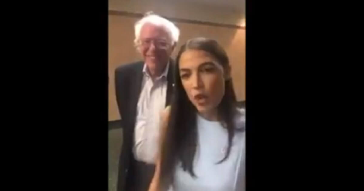 Ocasio-Cortez in the foreground with Bernie Sanders behind her.