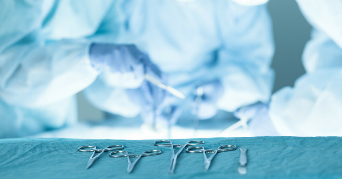 Surgeons hover over an operating table with tools in the foreground