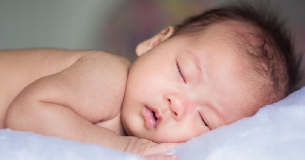 A baby sleeps on a white blanket.