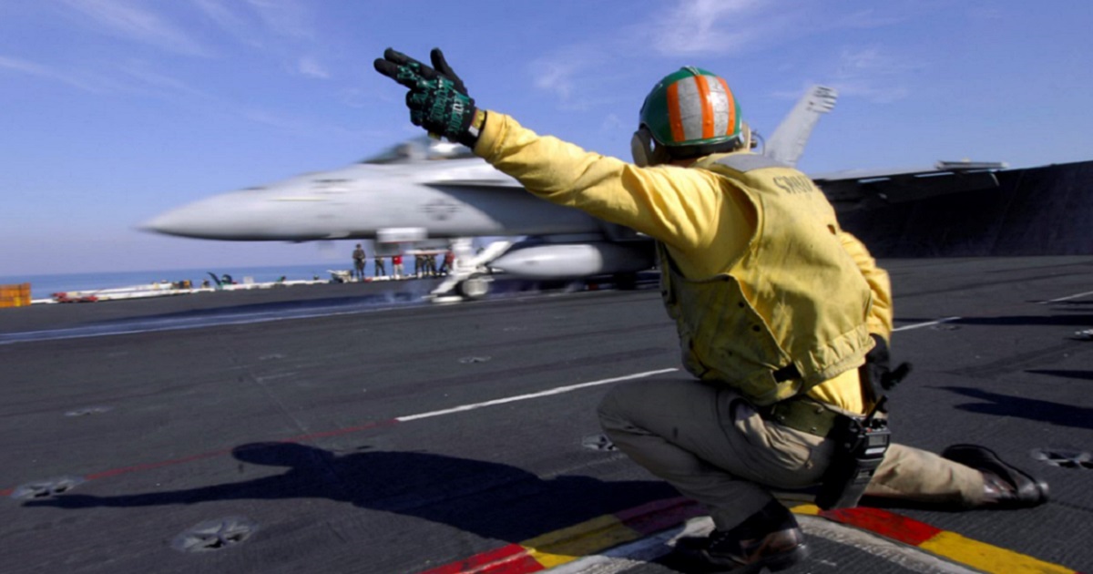 A crewman signals to plane in the background.