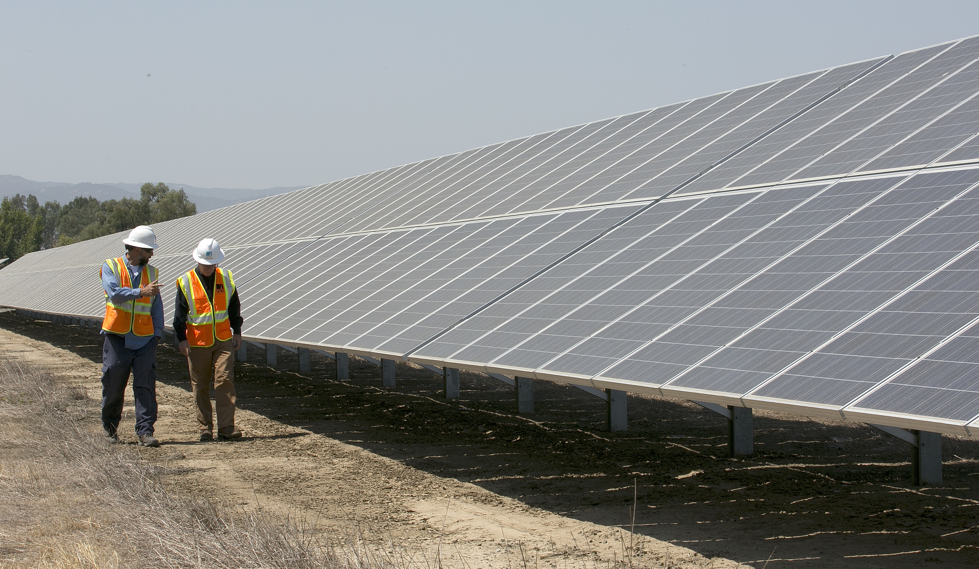 In this Aug. 17, 2017 file photo Solar Tech Joshua Valdez, left, and Senior Plant ManagerTim Wisdom walk past solar panels and at a Pacific Gas and Electric Solar Plant, in Vacaville, Calif. When California lawmakers return from their summer recess in August 2018, among the high-profile bills to consider is whether to bump up renewal energy mandates and setting a goal of getting all of California's energy from carbon-free sources by 2045.