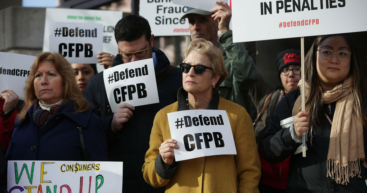 Supporters of the Consumer Financial Protection Bureau hold signs as they gather in front of the agency