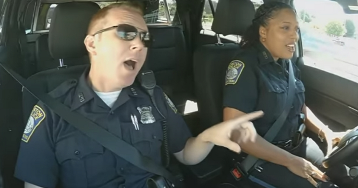 Two police officers sing God Bless America in their patrol car.
