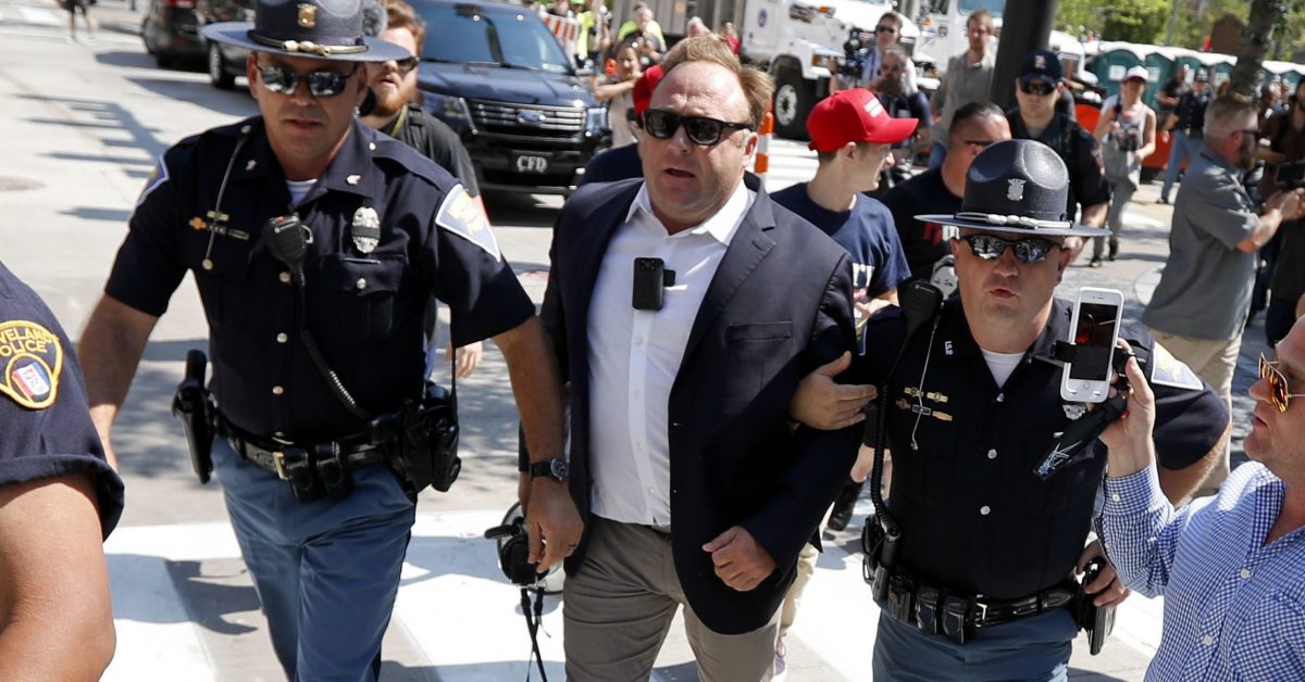 In this Tuesday, July 19, 2016 file photo, Alex Jones, center right, is escorted by police out of a crowd of protesters outside the Republican convention in Cleveland.