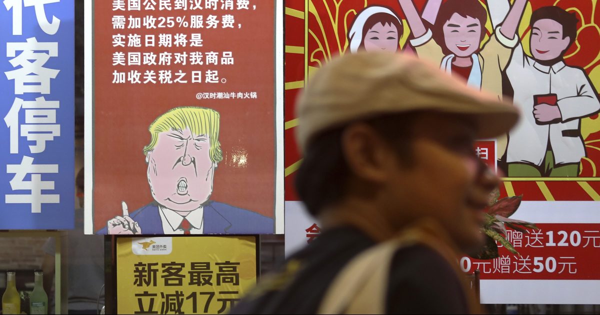 a man walks by a poster depicting a mural of U.S. President Donald Trump stating that all American costumers will be charged 25 percent more than others starting from the day president Trump started the trade war against China, on display outside a restaurant in Guangzhou in south China's Guangdong province.