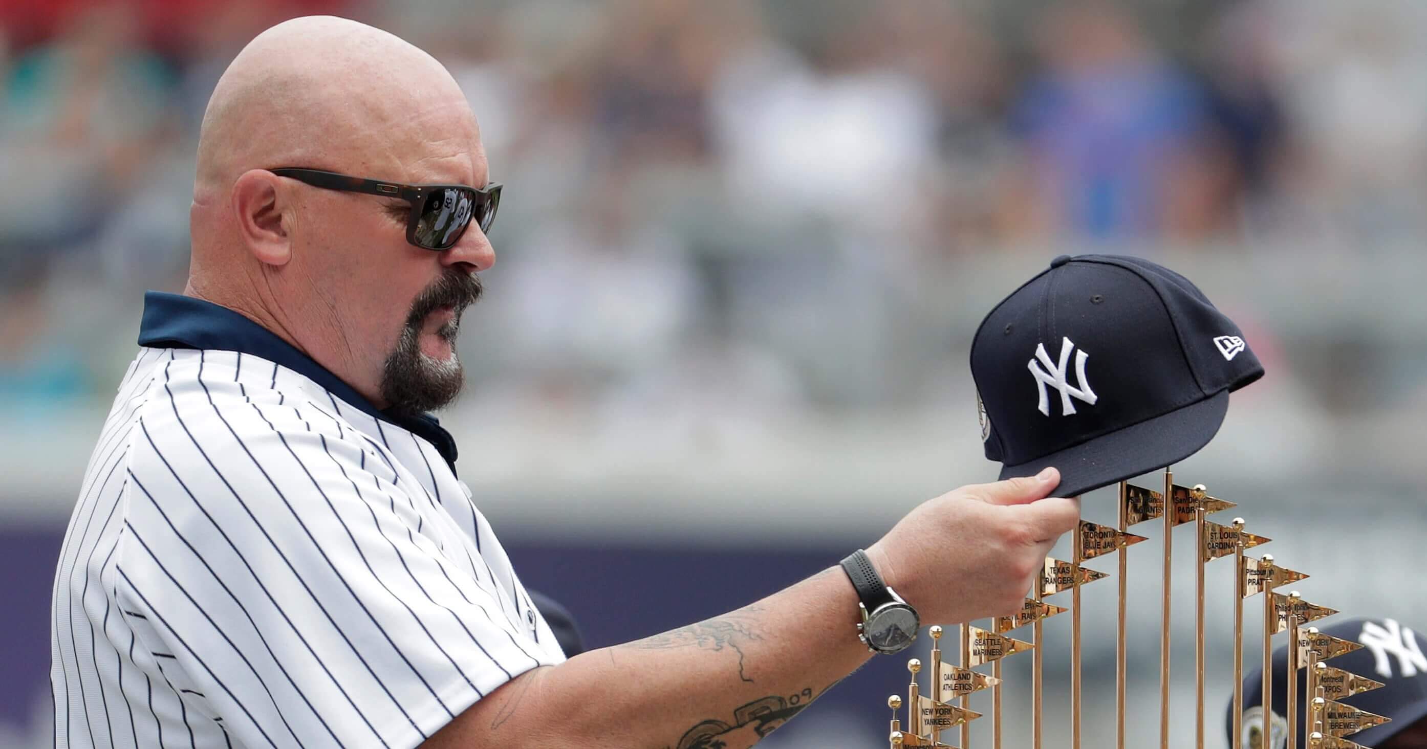 Former New York Yankees pitcher David Wells puts his hat on the 1998 World Series trophy during a ceremony honoring the team prior to a baseball game between the New York Yankees and the Toronto Blue Jays Saturday in New York.