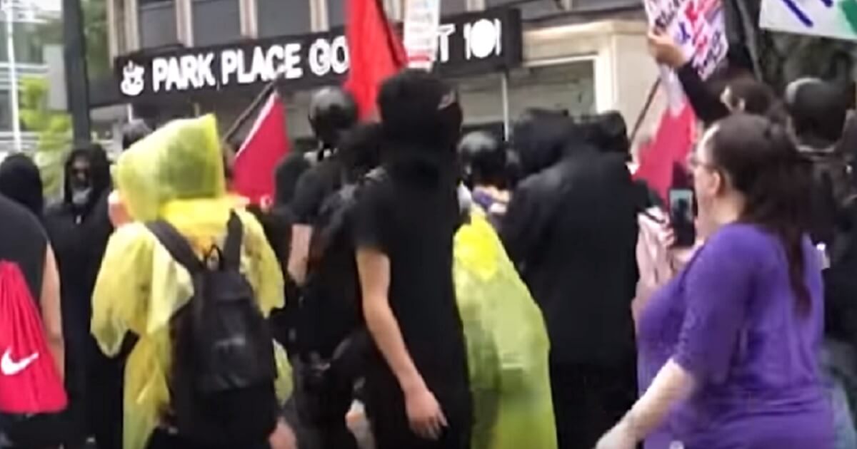 Man in black hood stands among marchers