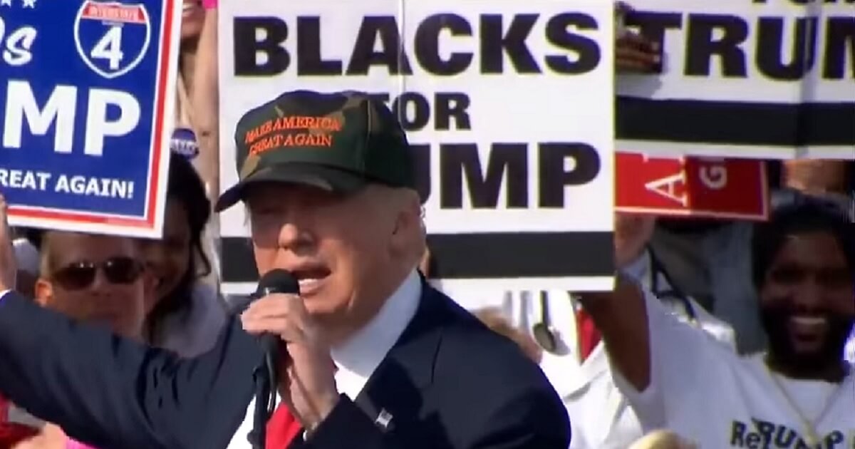 Trump at rally with "Blacks for Trump" sign in background.