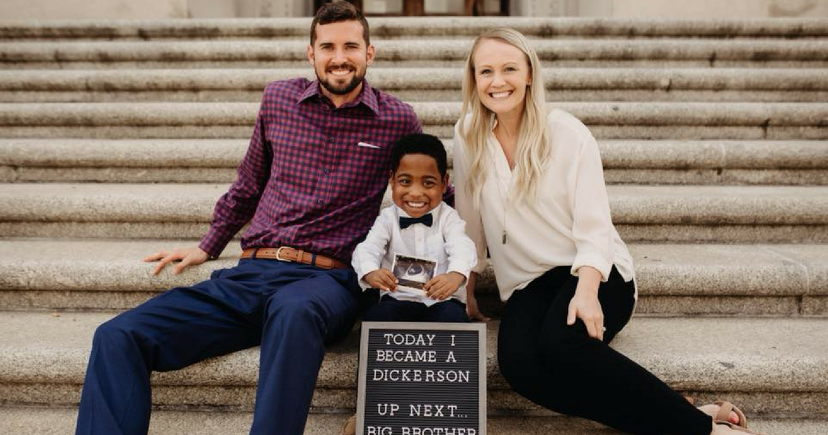 A family of three holds a sign announcing their son's adoption and their pregnancy