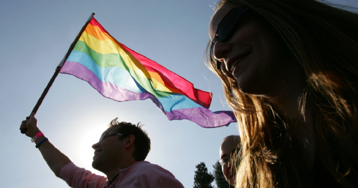 A rainbow flag is held aloft.