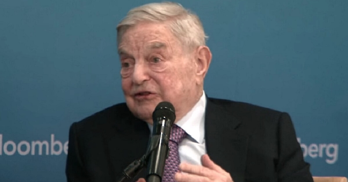 A seated Soros speaks into a microphone
