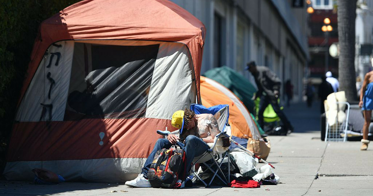 A homeless man sleeps in front of a tent in San Francisco