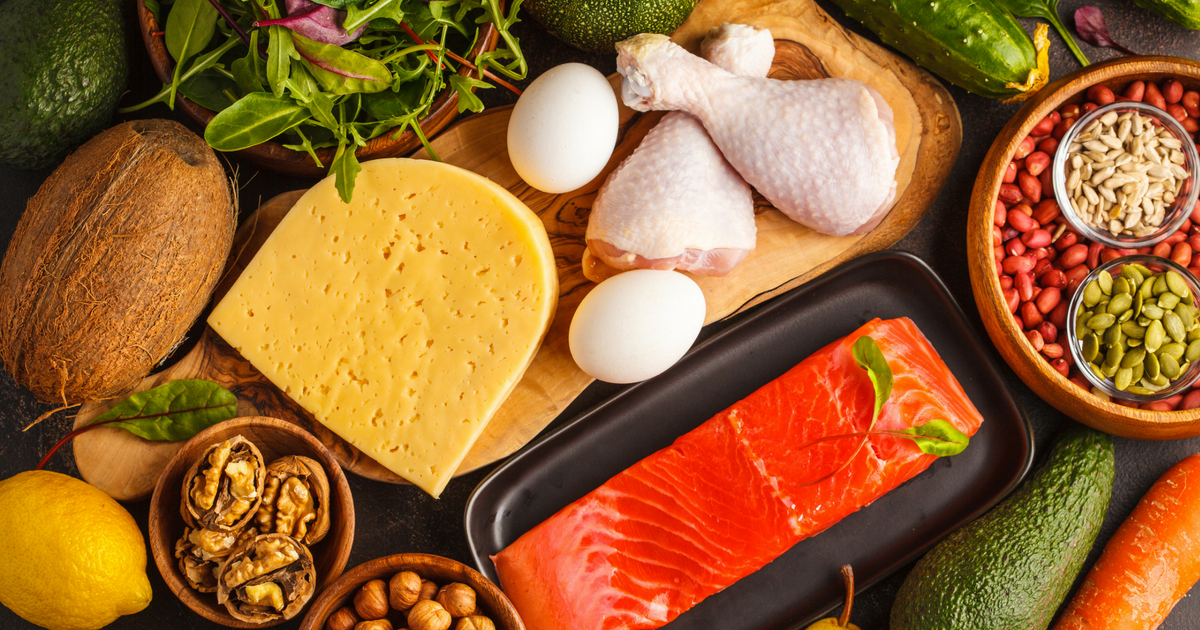 Ketogenic diet food -- vegetables, fish, meat, cheese and nuts -- displayed on a dark background.