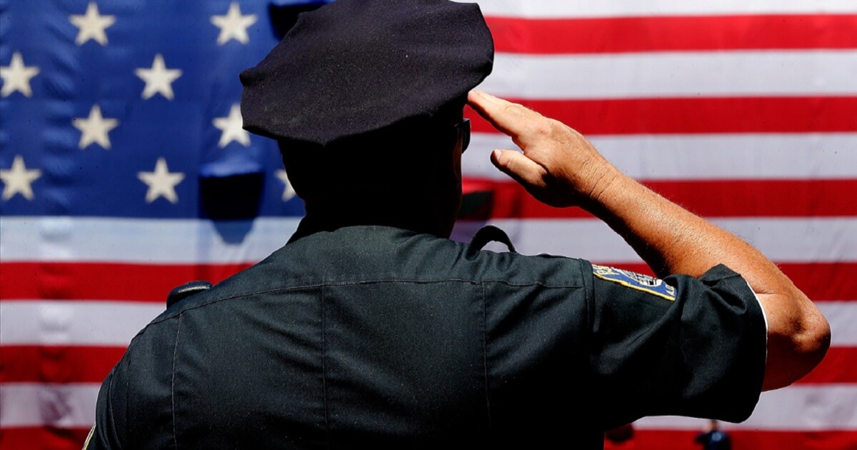 Officer saluting in foreground, facing flag in background.