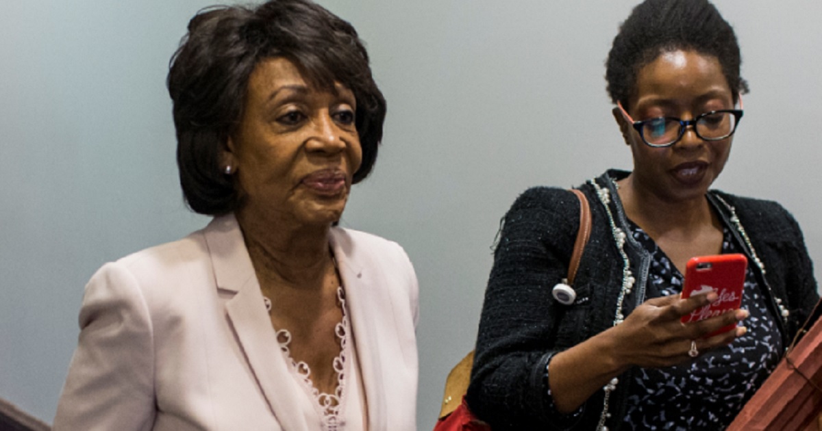 Maxine Waters strides through a hallway with a woman who appears to be an aide.