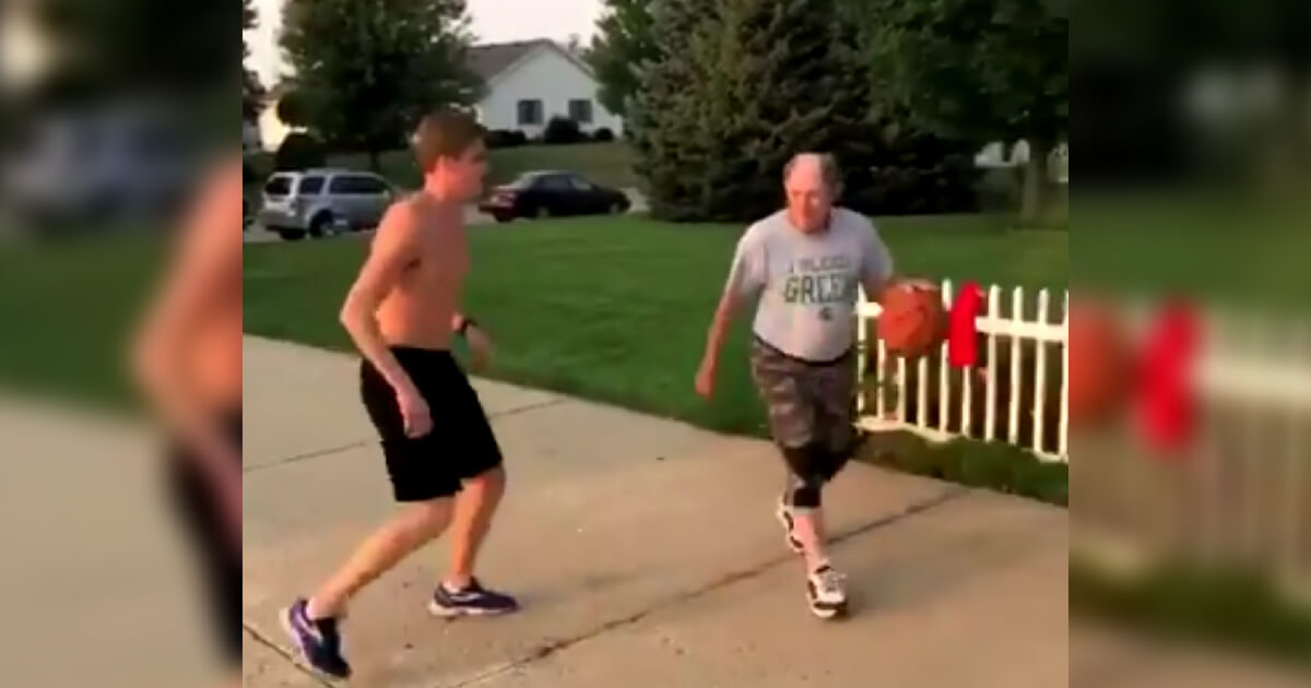 An older guy with two knee braces schools a youngster in one-on-one driveway basketball.