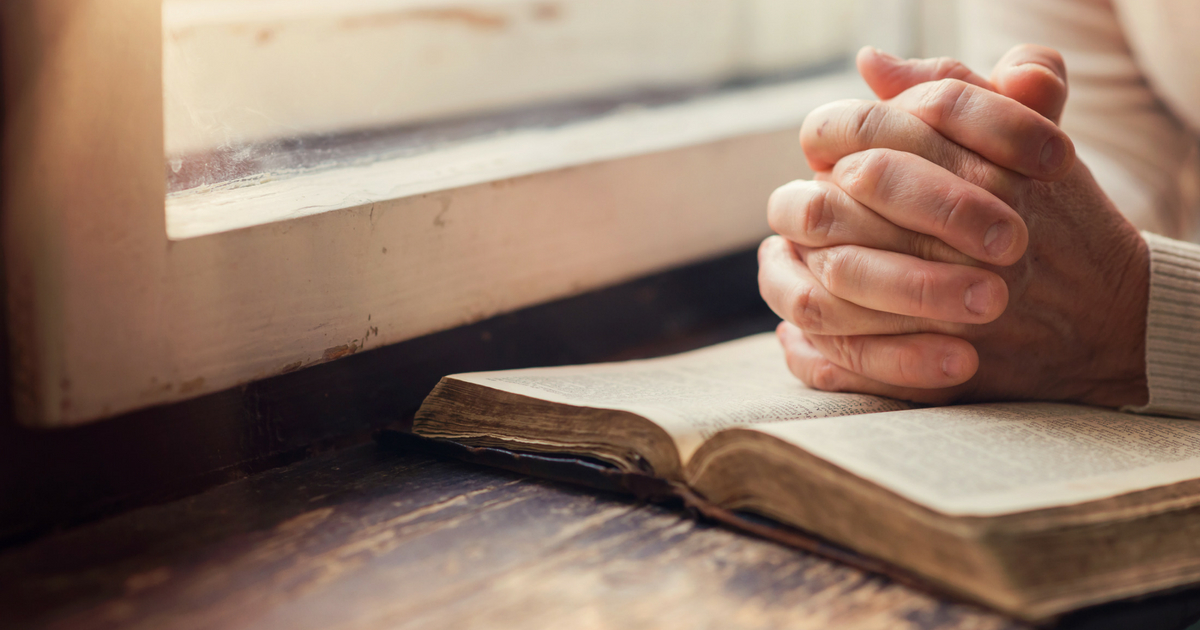 Hands clasped in prayer over an open Bible.