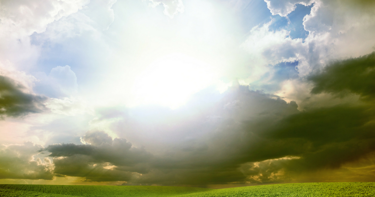 Bright sunshine is seen through clouds over a green field.