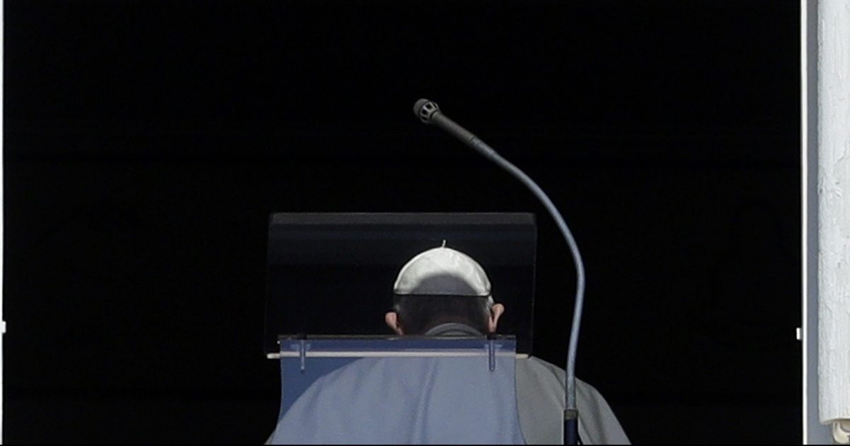 Pope Francis is viewed from behind against a dark backdropo.