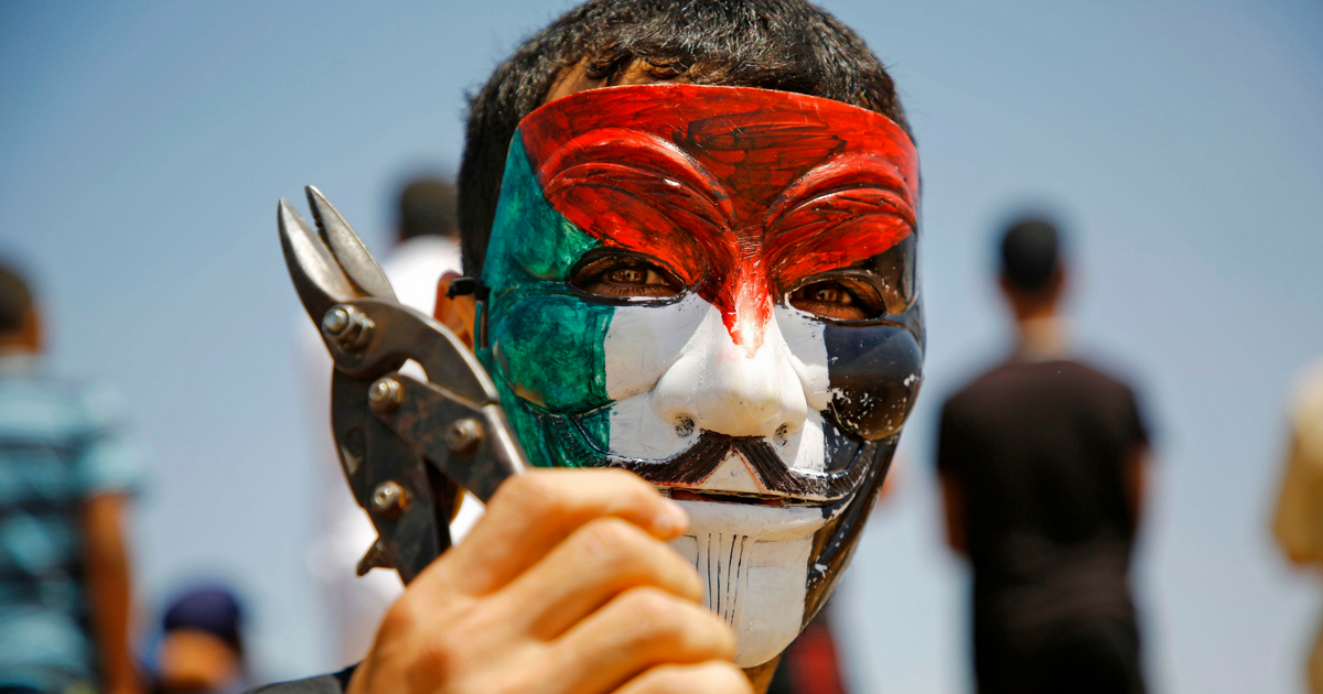 A Palestinian protestor wearing a Guy Fawkes mask coloured with the Palestinian flag poses while holding a wirecutter