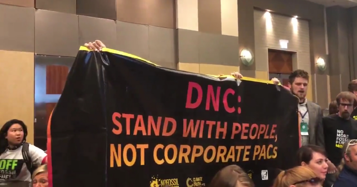 Protesters interrupting the DNC’s Resolutions Committee meeting to urge the DNC, through song, to reinstate Nancy Pelosi’s measure that bars fossil fuel industry corporate PAC money.