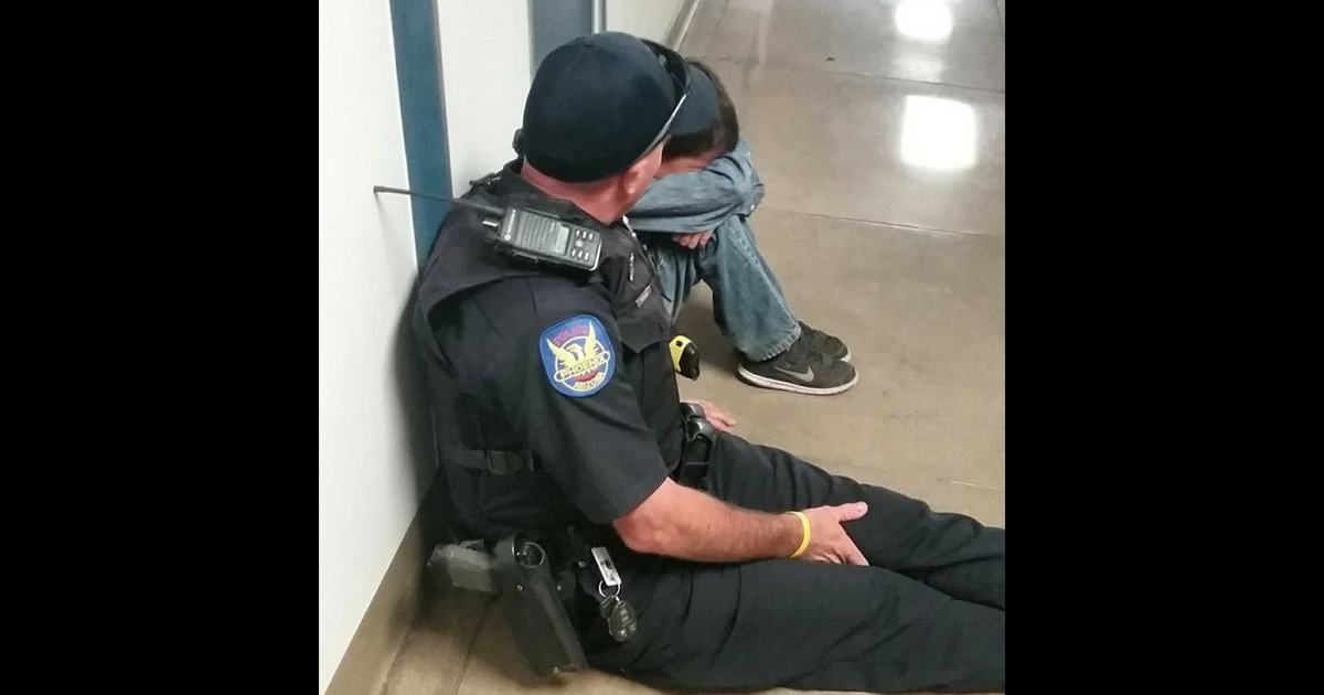 A resource officer sits down next to a crying child and comforts him.