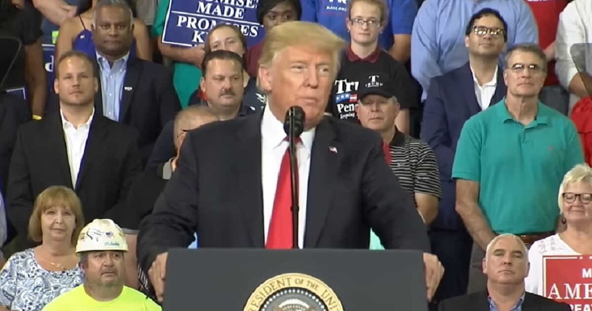President Trump at a podium with a crowd of supporters in the background.
