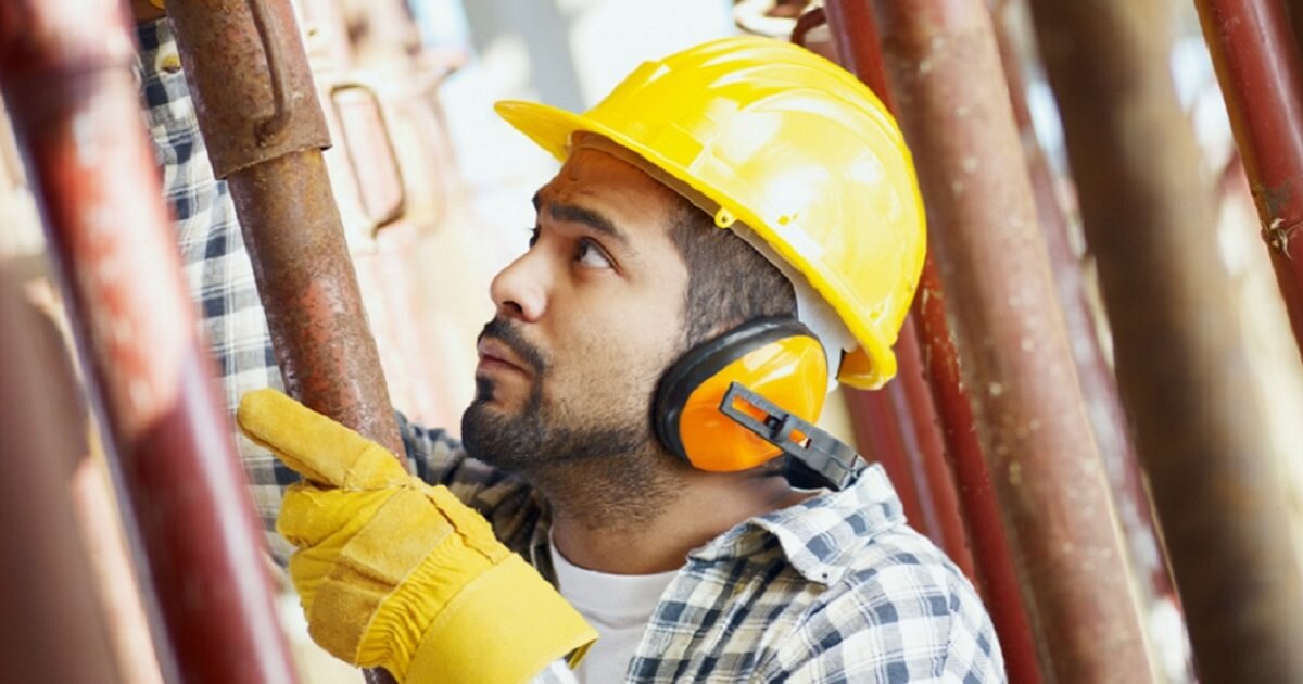 Man wearing hard hat and gloves works in a construction job.