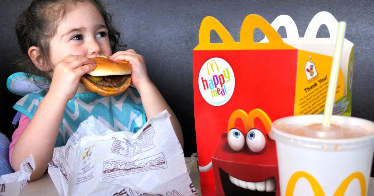 A young girl eats a hamburger from her kids meal at McDonald's