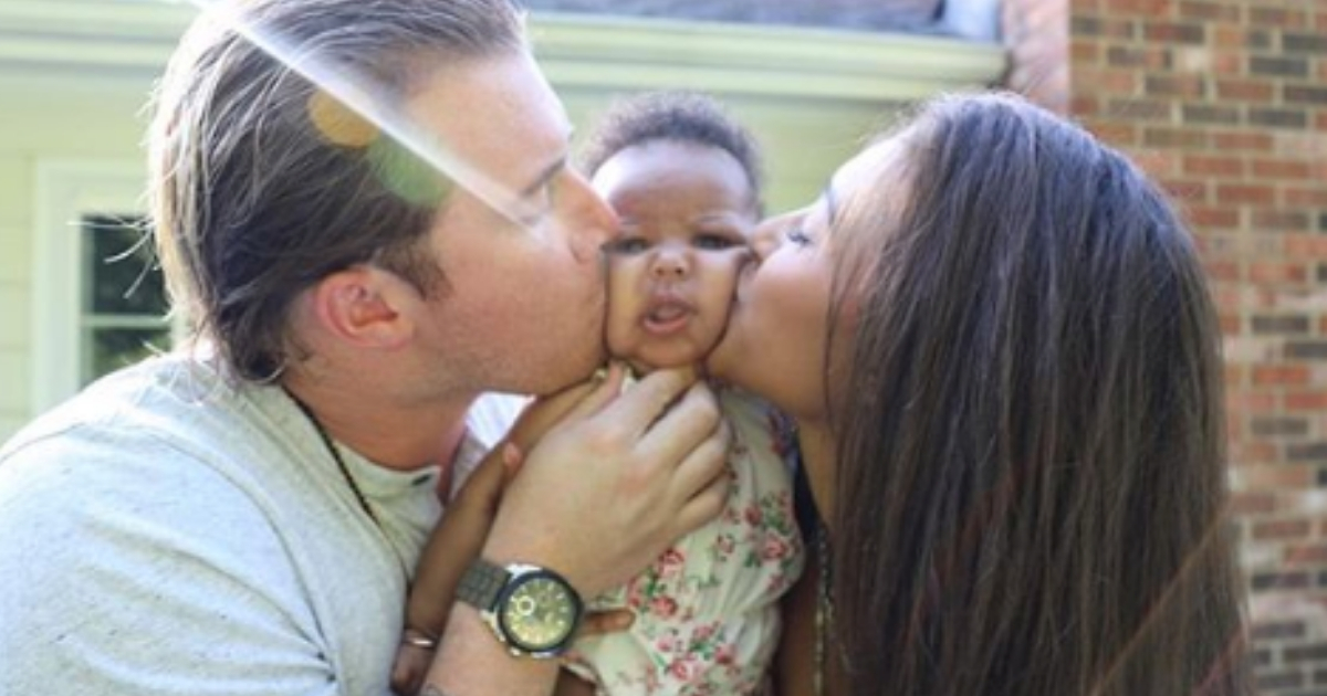 A mom and dad kiss their baby girl on her cheeks
