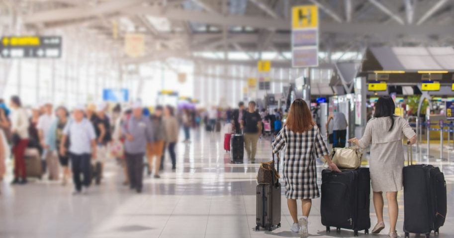 Two women carry luggage at the airport terminal.