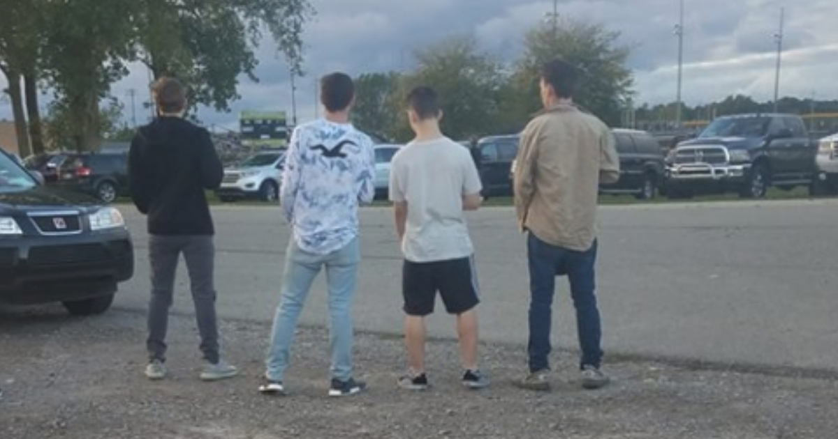 Four boys standing in the middle of a parking lot as the national anthem plays.
