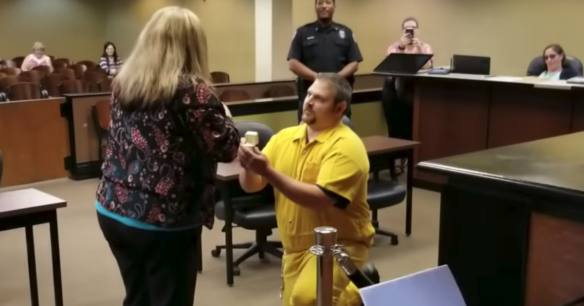 Man in yellow prison jumpsuit proposes to his girlfriend.