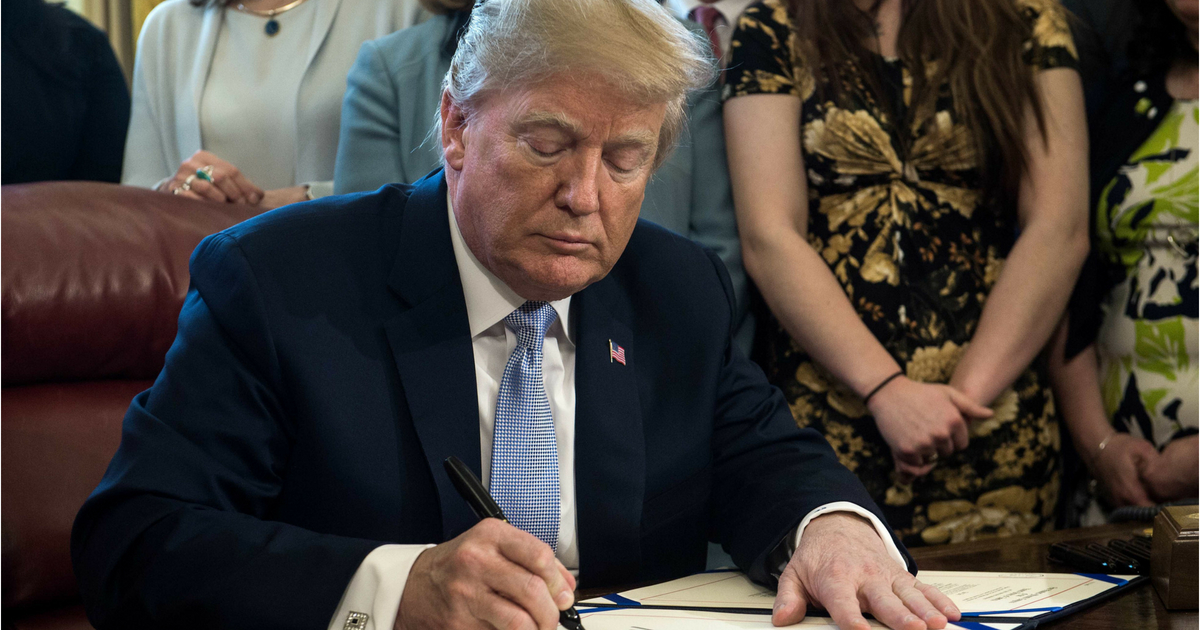 Donald Trump signs act at desk in Oval Office