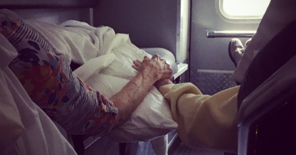 Elderly couple holding hands in the back of an ambulance.