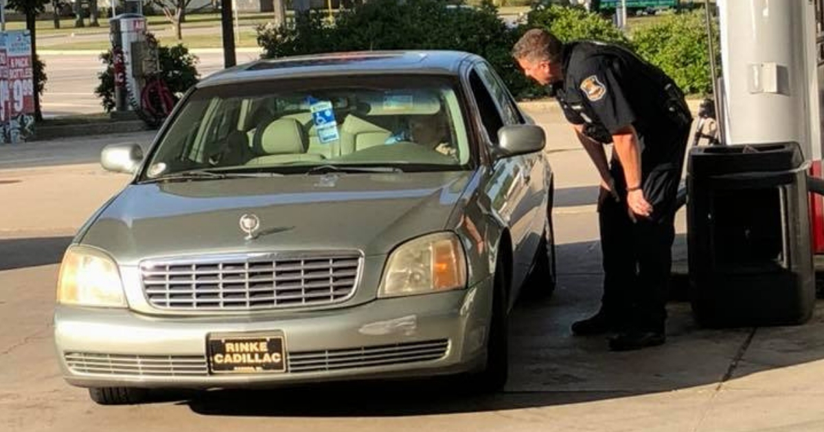 Police officers leans down to talk to an elderly woman in her car at a gas station.