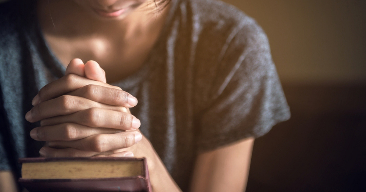 Woman praying with her hands together over a closed Bible.