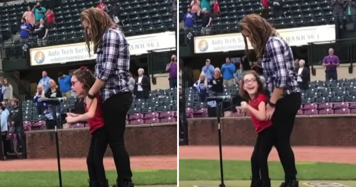 A mom helps her daughter stand in front of a microphone and sing the national anthem.