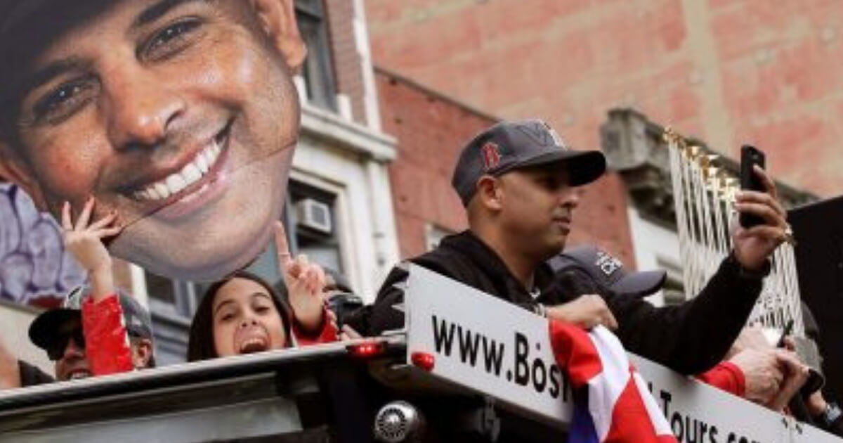Boston Red Sox manager Alex Cora takes a photo as his daughter Camila, left, holds a cutout photo of him during a parade to celebrate the team's World Series championship Wednesday in Boston.